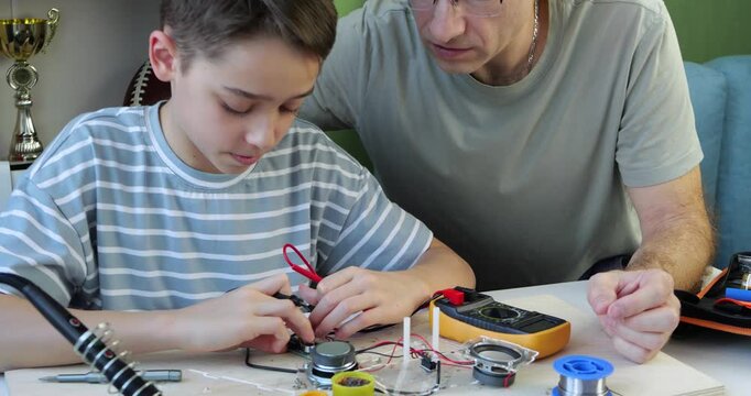 Father teaches son about electronics. Dad and boy explore circuit components and tools together. Both focus intently on the task, fostering learning and creativity. Hands-on experience enhances their