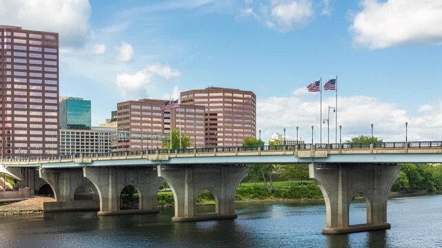 Panning timelapse of the Hartford skyline from across the Connecticut River on a sunny day, showcasing downtown buildings, the waterfront, and the capital of Connecticut.