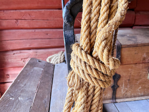 Coiled natural rope wrapped around rustic forged metal hook beside weathered wooden bench in traditional outdoor setting closeup texture nautical equipment handmade fiber material twisted strands mari