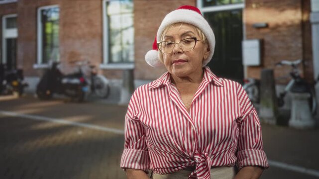 Woman wearing santa hat and glasses standing facing camera on street in front of brick building and bicycles; nostalgia holiday.