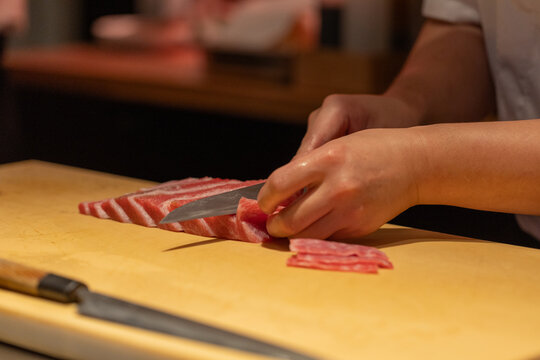 Skilled chef slicing fresh fish on wooden cutting board in kitchen