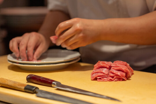 Skilled chef preparing thinly sliced meat on wooden cutting board