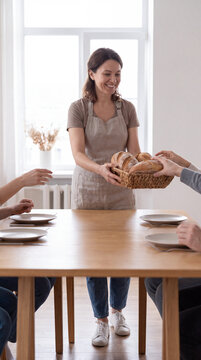 Smiling woman passing warm bread basket to guests at community dinner table