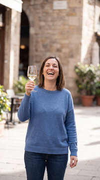 Woman laughing while raising wine glass to toast in charming old town plaza