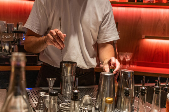 Bartender mixing cocktails at bar with shiny tools and vibrant lighting