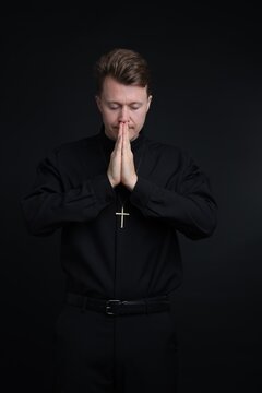 Priest in cassock praying on black background