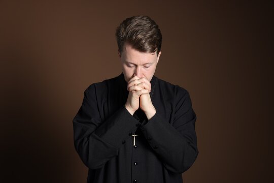 Priest in cassock praying on brown background