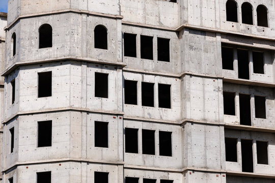 Unfinished multi-story concrete building facade with empty windows under bright sunlight