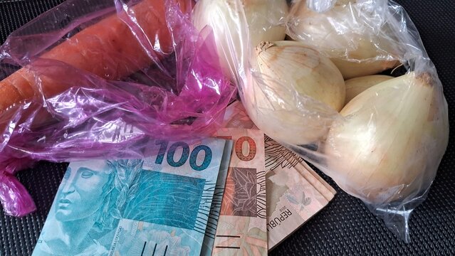 Fresh raw onions and carrot placed beside brazilian real bank notes