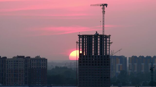 Skyscraper building under construction with tower crane against bright pink sunrise sky time lapse. High rise residential architecture in urban cityscape.