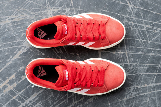 Red Adidas sneakers aligned horizontally on a scratched gray surface from above.