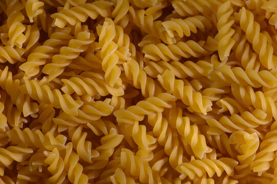 Commercial food photography of a macro top-down background of dry fusilli pasta with moody shadows