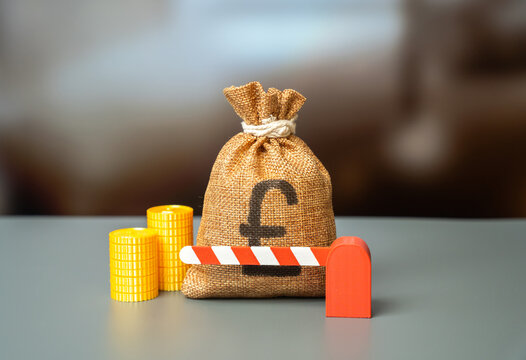 The British pounds money bag is blocked by a closed barrier. Freezing of funds and accounts. Prevent money laundering. Government lockdown and halt in funding. Sanctions and capital embargoes.