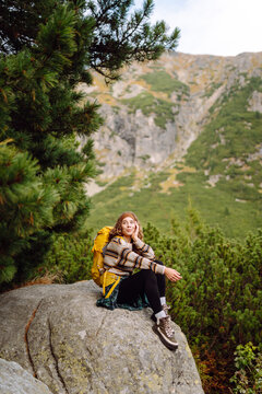 A woman with a hiking backpack enjoys a hike along a rocky mountain trail. The hiker takes in the mountain scenery at sunset. Concepts: adventure, nature, active lifestyle.