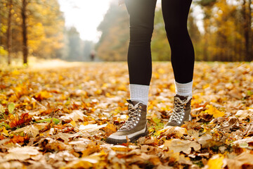 Person in boots walks along forest path surrounded by bright fallen leaves at sunset. Close-up shot...