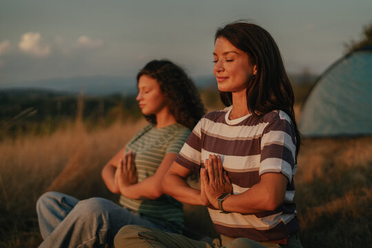 Two women meditating in nature during sunset camping trip