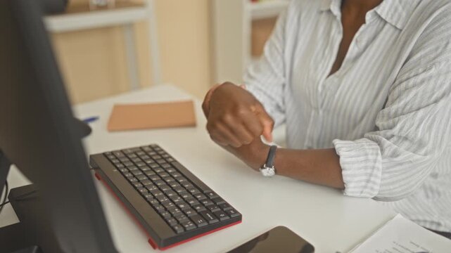 Woman massaging wrist at computer keyboard on office desk in building, middle age business worker holding wrist after typing; discomfort.