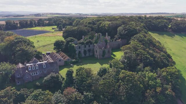 Aerial orbit view of historic ruined Seacliff House surrounded by dense forest in East Lothian Scotland