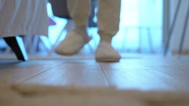 Woman's feet wearing warm slippers at home. Low-angle shot of female feet wearing cozy white slippers walking on a wooden floor, a perfect representation of comfort, relaxation, and a cozy home