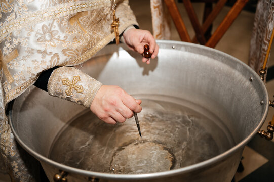 Priest blessing the water in a baptismal font with holy oil