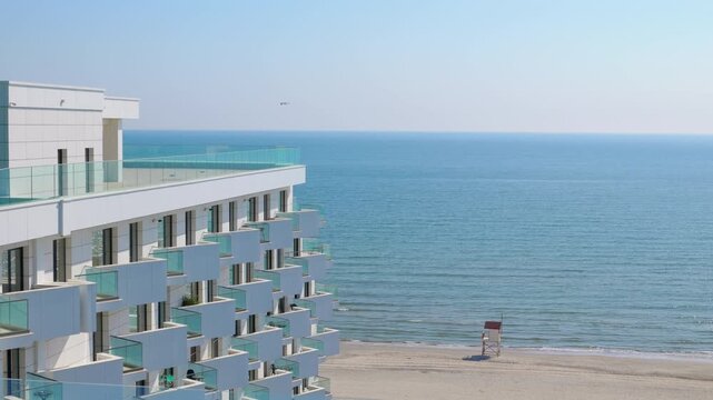 Modern beachfront hotel overlooking the calm ocean. Sunny day view of a contemporary white hotel with multiple balconies directly on a sandy beach, featuring a serene ocean background