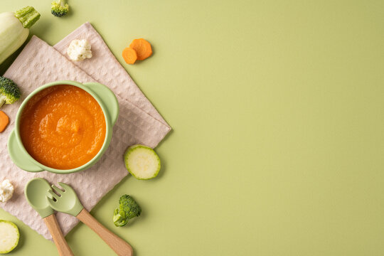 Baby first feeding with healthy vegetable puree in bowl and wooden utensils on pastel background