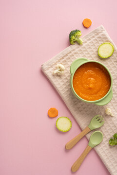 Baby first feeding with healthy vegetable puree in a green bowl on a vertical pink background