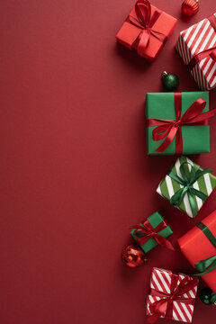 Merry Christmas and happy New Year flat lay with red and green wrapped presents and ornaments on vertical burgundy copyspace