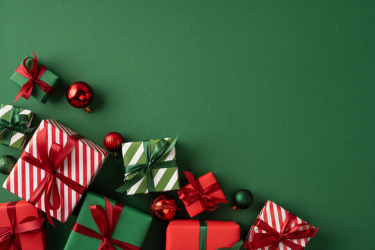 Merry Christmas gift display with red and green wrapped presents, ribbons and baubles for Happy New Year on green backdrop