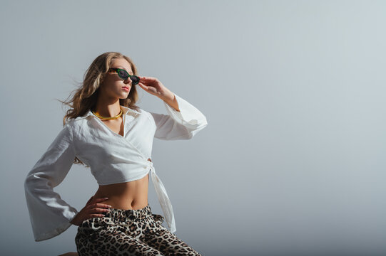 Fashionable confident woman wearing trendy green color sunglasses, white linen wide sleeve blouse, chunky golden necklace, posing in studio. Fashion portrait. Copy, empty space for text