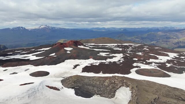 Stunning aerial pan left view of the volcanic landscape on Iceland, showcasing the 2 volcanos Magni and M&oacute;&eth;i on the Fimmv&ouml;r&eth;uh&aacute;ls trail. Remote, red, rugged terrain with snow patches.
