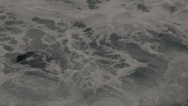 Black Rock Protruding from White Foamy Rough Waves
