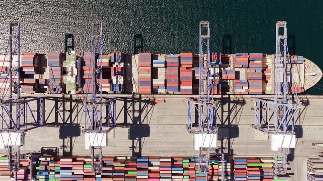 Industrial port scene featuring a large cargo ship docked at a terminal while massive cranes unload colorful intermodal containers, showcasing global trade and maritime shipping logistics