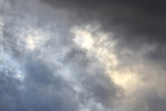 Sunlight breaking through dark storm clouds in dramatic grey sky background