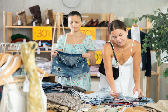 Observant young female customers reviewing casual pantaloons during shopping in clothing store