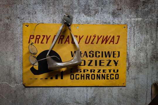Vintage Polish workplace health and safety warning sign with protective goggles hanging on concrete wall
