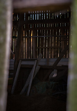 Sunlight filtering through wooden slats into dark rustic old barn interior