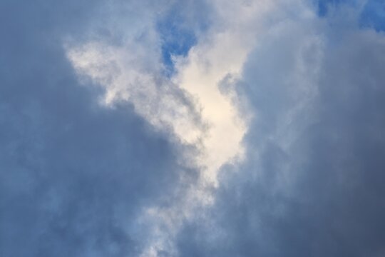 V shaped break in dark storm clouds with sunlight breaking through blue sky