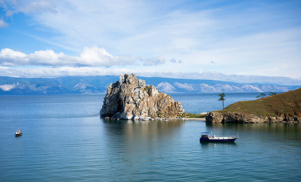 Landscape of Shamanka rock on Lake Baikal in Russia. Passenger boat navigating near Olkhon island coast with mountains in background. Summer travel destination