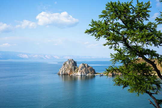 Landscape view of Shamanka Rock on Lake Baikal, Russia. Two-peaked stone island in blue water framed by a green coniferous tree. Summer travel destination in Siberia