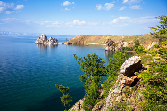 Landscape view of Lake Baikal and Shamanka Rock on Olkhon Island. Summer scenery with deep blue water, rocky cliffs, and green trees. Natural travel destination background
