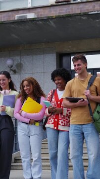 Vertical. Happy multiracial group of college students laughing and talking on the stairs of the campus building, showcasing friendship and the academic lifestyle in a university setting
