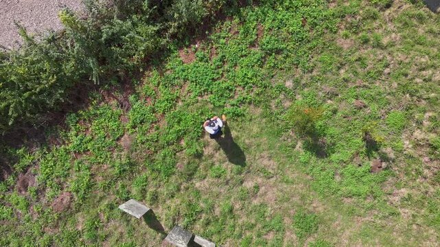 An aerial view captures a lone male photographer standing amidst old gravestones and lush green grass. The camera rises and spins, looking down upon the scene near the River Fowey in Cornwall