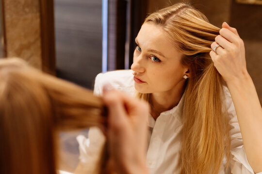 Woman studying hair condition in close mirror view for self-care. The close composition centers attention on hair condition.