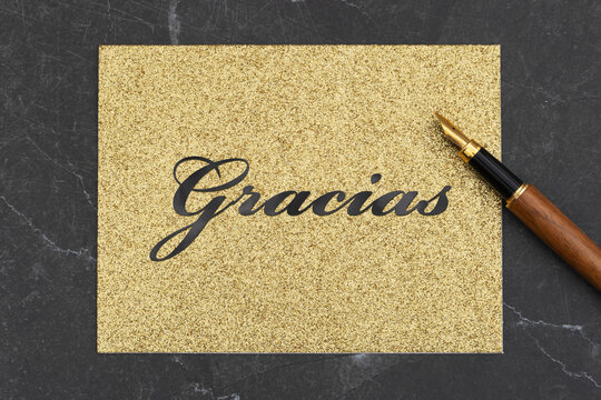 Thank you Gracias Spanish message on gold glitter greeting card with pen on black stone
