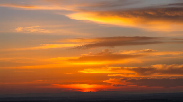 Sunset sky displaying warm golden and orange clouds over a dark distant horizon.