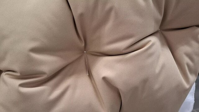 Beige upholstered cushion with deep tufting in close view. Home comfort, interior decor, soft furniture, cozy living, textile detail.