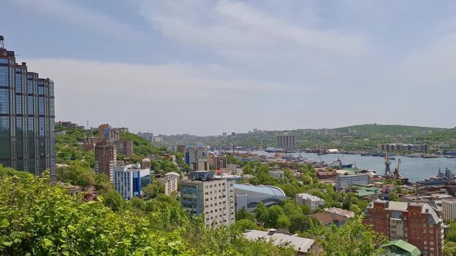 Modern skyscraper stands on green hill in Vladivostok, Russia. Cityscape skyline, urban architecture development, maritime city travel. City buildings on hillside overlooking sea. Coastal skyline