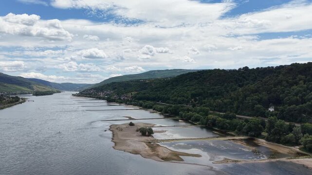 Aerial view of the Rhine River near Bacharach, Germany, showing exposed gravel bars, forested hills and the scenic Middle Rhine Valley beneath a dramatic summer sky