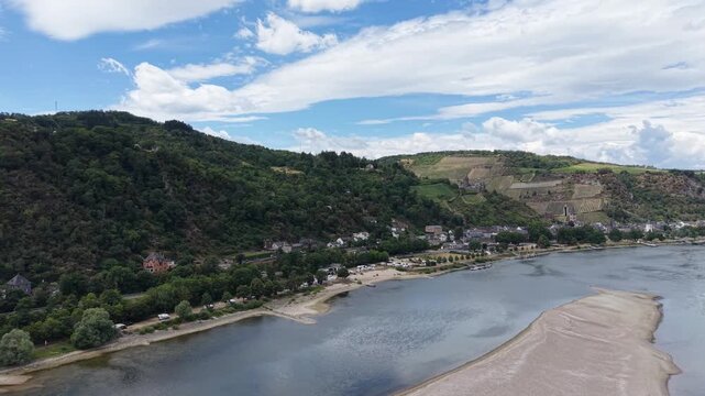 Aerial view of the Rhine River near Bacharach, Germany, with hillside vineyards, traditional houses and historic architecture surrounded by green landscape in the Upper Middle Rhine Valley.